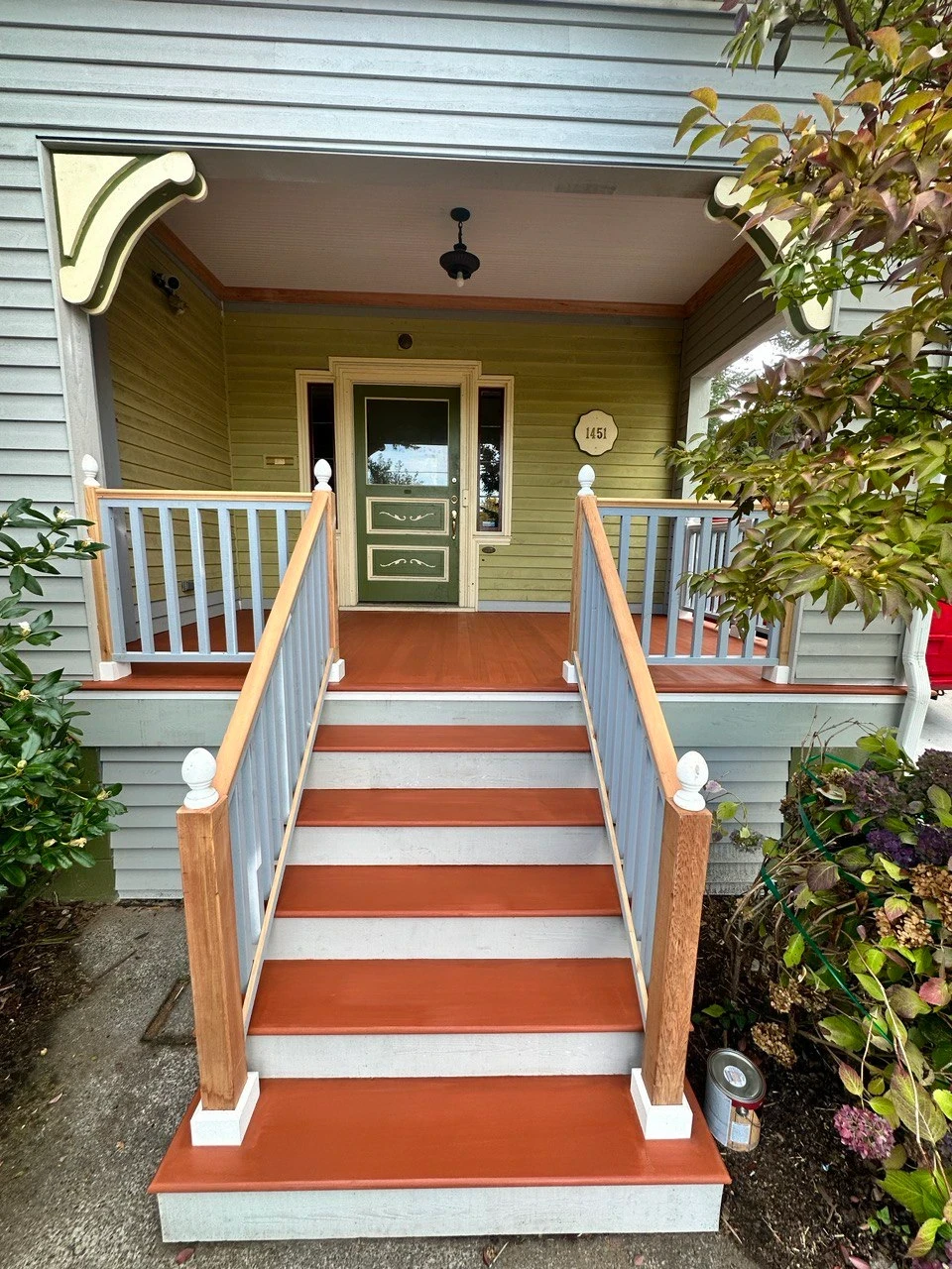 Rebuilt treads in a warm terracotta finish against gray risers, with fresh wood-and-gray railing framing the entry.